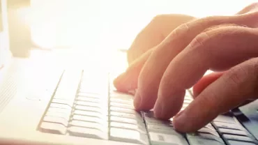 Mains tapant sur un clavier d'ordinateur portable à la lumière.