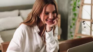 Woman smiling at a laptop in a cozy, modern living room.