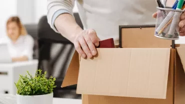 Person packing office supplies into a cardboard box.