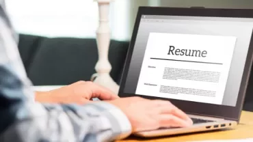 Person typing a resume on a laptop at a desk.