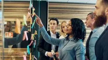 Team discussing in front of a glass wall with sticky notes.