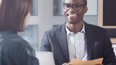 Two people having a meeting in an office setting, one holding a folder and smiling.