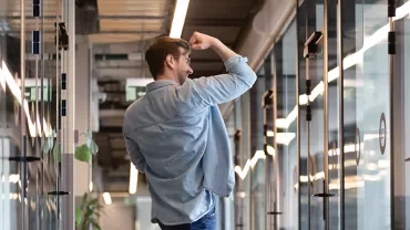Man celebrating in modern office hallway.