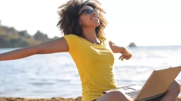 Woman in yellow shirt enjoying beach with laptop
