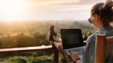 Person working on a laptop with a scenic view at sunset.