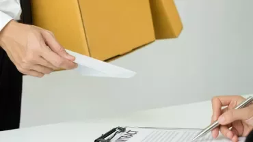 Person handing a document to another person signing a contract.