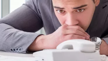 Man in a suit looking pensively at a desk phone.