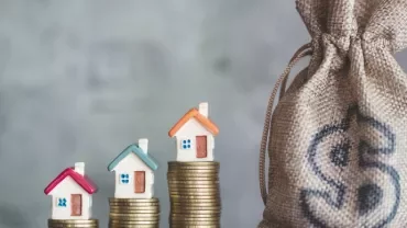 Small houses on coin stacks beside a money bag.