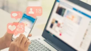 Person using a smartphone with social media notifications, next to a laptop.