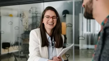 Woman in glasses smiles while shaking hands in a modern office.