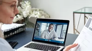 Woman video conferencing with a man, holding a resume.