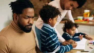 Family working together in the kitchen with a laptop and notebooks.