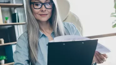 Femme avec des lunettes examinant des documents à son bureau.