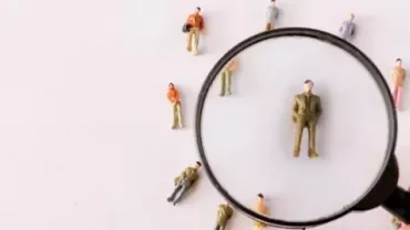 Magnifying glass focuses on miniature figure surrounded by others.