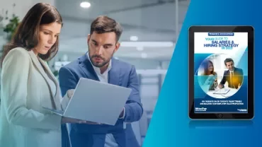 Two professionals discussing at a laptop with a hiring strategy guide on a tablet screen.