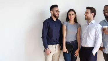 Group of four people smiling and standing against a white wall.