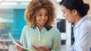 Two women talking and one holding a sheet of paper