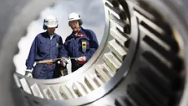Two workers in protective gear examining machinery parts.