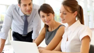 Three colleagues collaborating at a desk with a laptop.