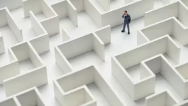 A businessman stands in a large white maze, contemplating his path.