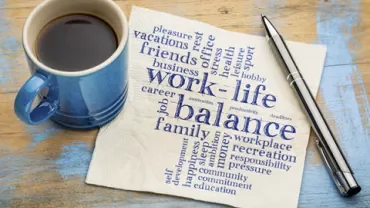 Coffee cup and pen next to napkin with 'work-life balance' word cloud.