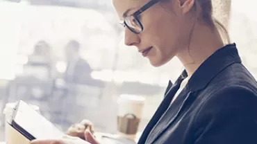 Woman with glasses reading a tablet in a coffee shop.