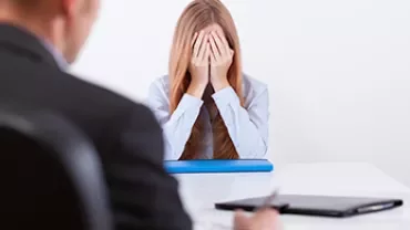 Personne à un bureau se couvrant le visage, semblant stressée.