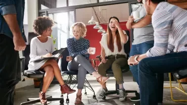 Group of colleagues laughing and talking in an office setting.