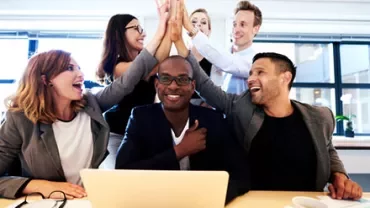 Group of colleagues celebrating a success with high-fives around a laptop.