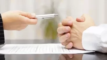 Deux personnes à une table, une tenant un stylo au-dessus d'un contrat.