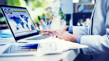 Person working on a laptop with graphs and maps displayed.