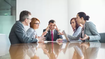 Business meeting with five people in discussion around a table.