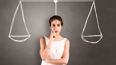 Woman contemplating in front of drawn balance scales on blackboard.