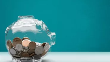 Transparent piggy bank filled with coins against a blue background.
