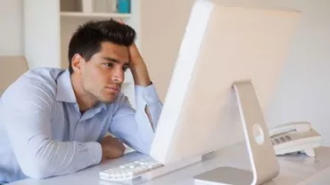 Man sitting at a desk, looking stressed at a computer screen.