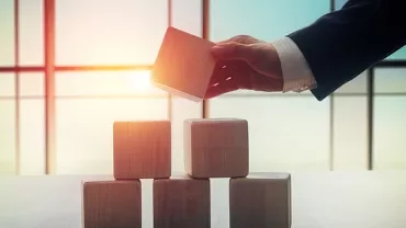 Hand placing a wooden block on a pyramid stack.