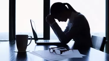 Silhouette of person stressed over laptop at desk with coffee mug.
