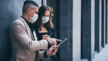 Two people wearing masks, discussing something on a tablet.