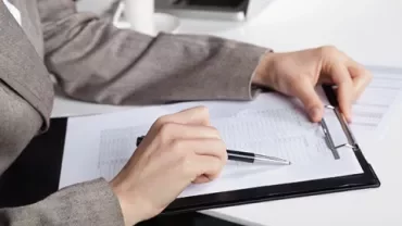Person reviewing documents on a clipboard at a desk.
