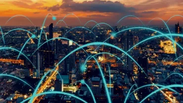 A city skyline at sunset with glowing digital network lines arching over buildings.