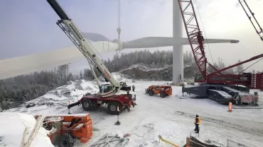 Workers installing a wind turbine blade with cranes in a snowy landscape.