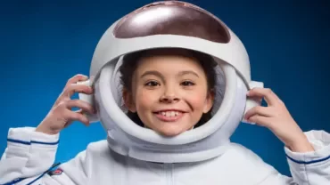 Child smiling in astronaut helmet against blue background.