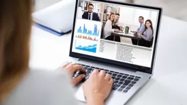 Person on a video call with graphs and meeting participants on a laptop screen.