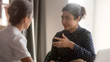 Two women having a discussion at a desk.