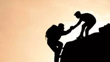 Two climbers silhouetted against a sunset, one helping the other up.