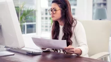 Woman at desk analyzing documents on computer.