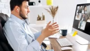 Homme en vidéoconférence à un bureau avec un écran d'ordinateur montrant plusieurs personnes.
