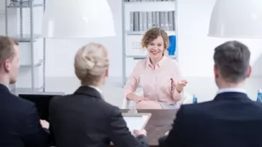 Woman speaking to interview panel in office setting.