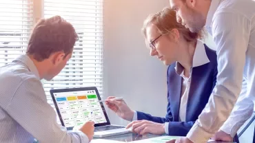 Three colleagues discussing a project on a laptop at a desk.