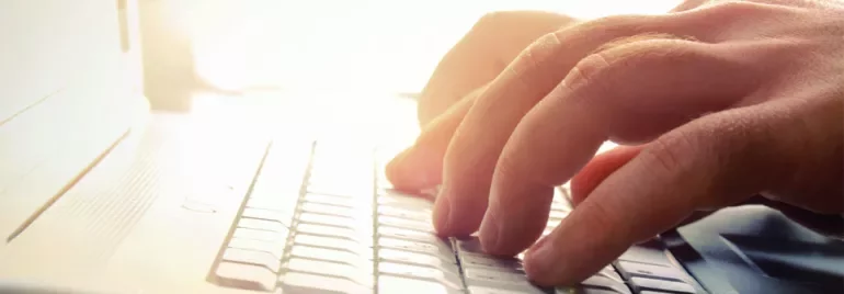 Mains tapant sur un clavier d'ordinateur portable à la lumière.